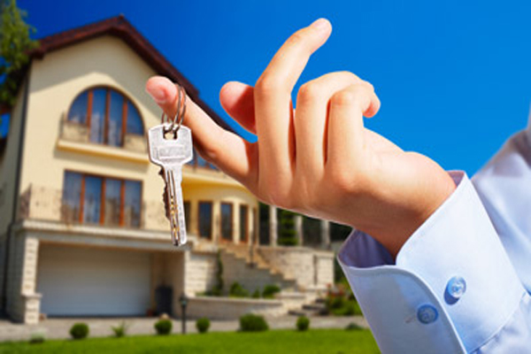 Hand holding house keys with a home in the background.