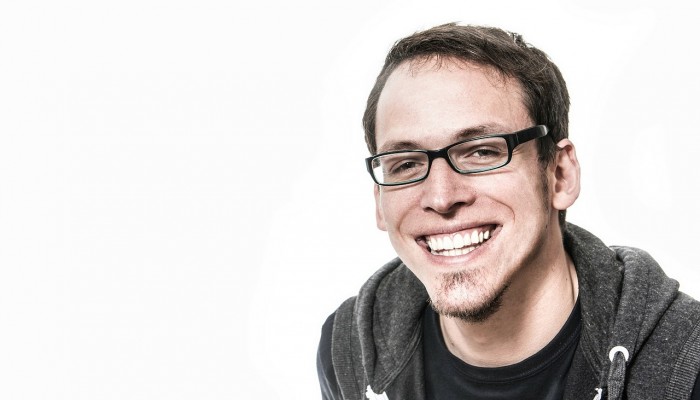 Smiling man with glasses and casual attire against white background.